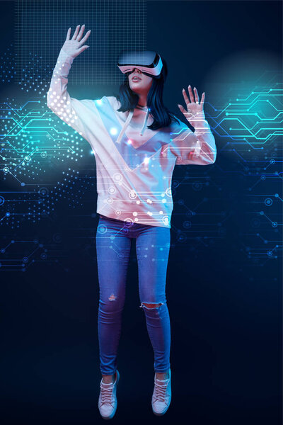young excited woman in virtual reality headset levitating in air among glowing data illustration on dark background 