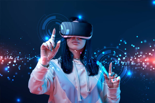 woman in virtual reality headset pointing with fingers at glowing cyber illustration on dark background