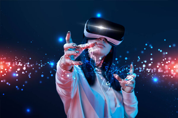 young woman in vr headset gesturing near glowing cyber illustration on dark background