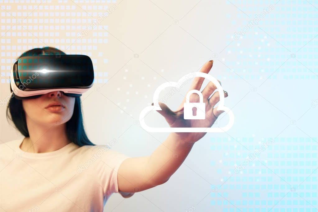 young woman in virtual reality headset pointing with hand at internet security illustration on beige and blue background