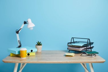 workplace with papers, succulent and coffee in plastic cup on wooden table on blue background