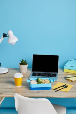 mavi arka plan, açıklayıcı editoryal ahşap masa üzerinde dizüstü bilgisayar ve kağıtları ile işyerinde pirinç ve tavuk ile sağlıklı öğle yemeği