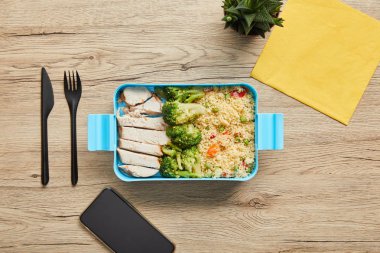 Ahşap masa üzerinde plastik öğle yemeği kutusunda sağlıklı besleyici risotto, sebze ve tavuk üst görünümü