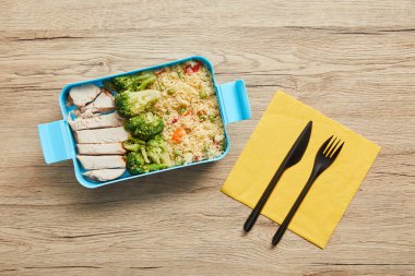 Ahşap masa üzerinde risotto, tavuk ve brokoli ile plastik öğle yemeği kutusunun üst görünümü