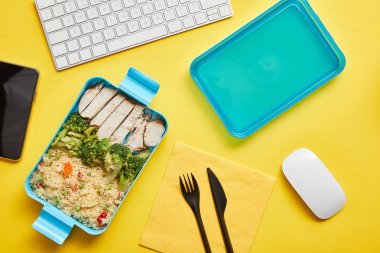 Plastik öğle yemeği kutusu ve sarı arka plan üzerinde bilgisayar klavyesi risotto ve tavuk ile lezzetli brokoli üst görünümü