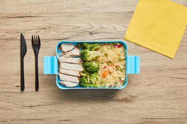 Ahşap masa üzerinde risotto, brokoli ve tavuk ile öğle yemeği kutusunun üst görünümü