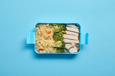 Mavi arka plan üzerinde lezzetli tavuk, risotto ve brokoli ile öğle yemeği kutusunun üst görünümü