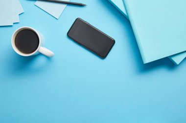 Mavi arka plan üzerinde işyerinde boş ekran ve kahve fincan ile akıllı telefon üst görünümü