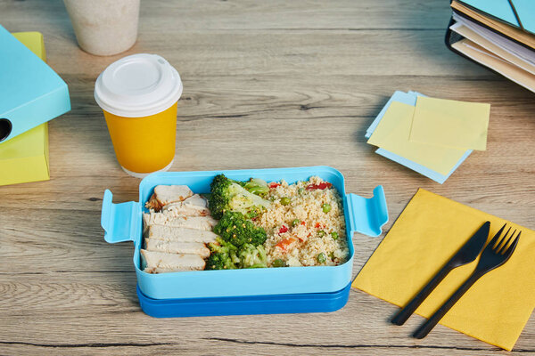 tasty risotto with chicken and coffee in plastic cup at workplace with folders and sticky notes on wooden table