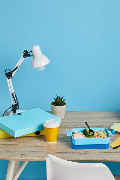 workplace with lamp, folders and tasty lunch on wooden table on blue background