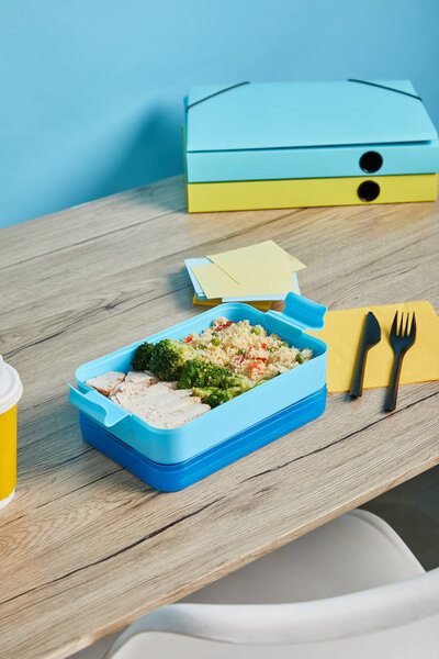 lunch box full of delicious rice with broccoli and chicken on wooden table on blue background 