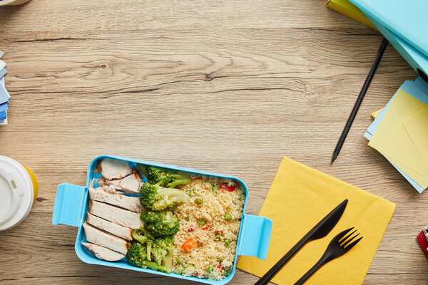 Top view of plastic lunch box with rice, broccoli and chicken on wooden table