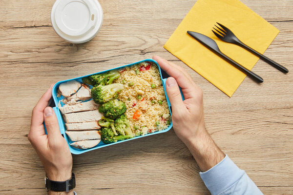 Cropped view of man sitting at table and holding lunch box with healthy and tasty food