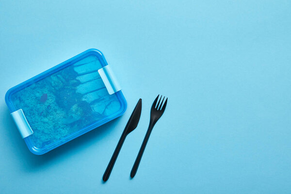 Top view of lunch box with healthy food and disposable fork and knife on blue background