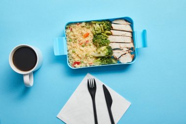 Mavi arka plan üzerinde risotto, tavuk ve brokoli ile bıçak ve öğle yemeği kutusu ile kahve fincanı, tek kullanımlık çatal üst görünümü