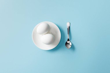 top view of teaspoon near boiled eggs on white plate on blue background clipart
