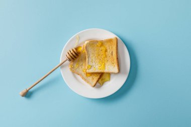 mavi arka plan üzerinde beyaz plaka üzerinde bal ve ahşap dipper ile tost üst görünümü 