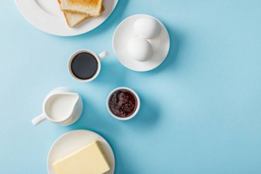 taze yumurta, reçel, tereyağı, kahve, süt ve mavi arka plan üzerinde beyaz tabaklar üzerinde iki tost üst görünümü
