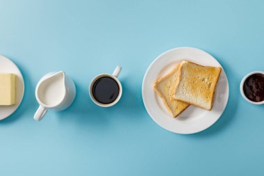 Kahve fincanı, süt, tereyağı, reçel ve mavi arka plan üzerinde beyaz tabak üzerinde iki tost üst görünümü