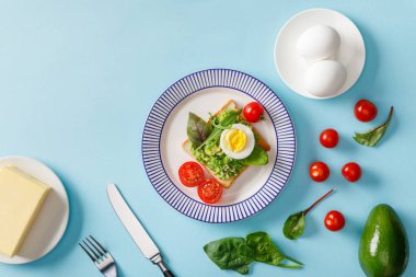 guacamole, avokado, haşlanmış yumurta, tereyağı, dağınık kiraz domates ve ıspanak mavi arka plan ile tost üst görünümü