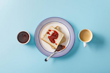 top view of toasts, spoon, bowl with jam and cup of coffee on blue background clipart