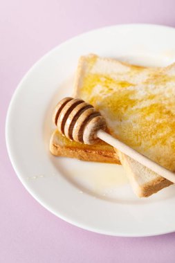 mor arka plan üzerinde beyaz plaka üzerinde bal ve ahşap dipper ile tost yakın görünümü