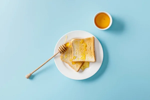 在蓝色背景的白色盘子上用蜂蜜和木制浸渍烤面包的顶视图 — 图库照片