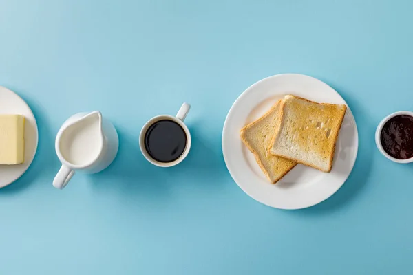 コーヒー ミルク バター ジャム 青い背景の白いプレート上の2つのトーストのトップビュー — ストック写真