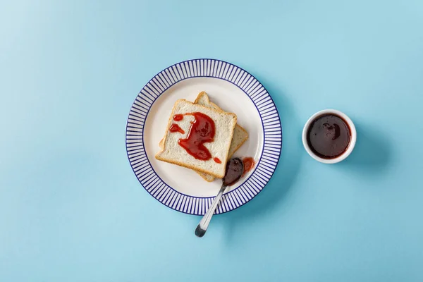 烤面包和勺子的顶视图与果酱在盘子靠近碗的蓝色背景 — 图库照片