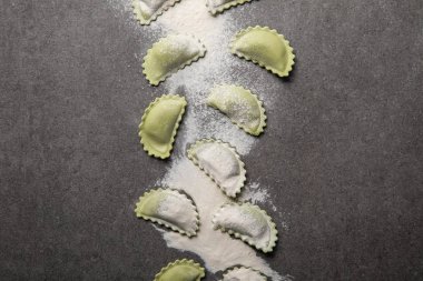 gri dokulu yüzeyüzerinde dağınık un ile ham yeşil ravioli üst görünümü