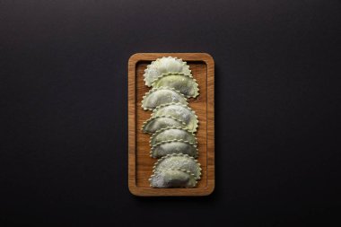 top view of raw green ravioli with flour on wooden board isolated on black clipart