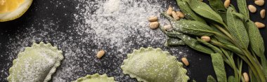 siyah arka plan üzerinde yeşil ham ravioli, çam fıstığı, ot ve un panoramik çekim