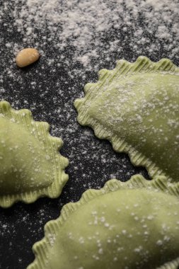 close up view of green ravioli with flour and pine nut on black table clipart