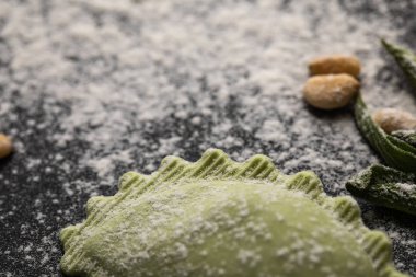 selective focus of green ravioli and scattered flour on black table clipart