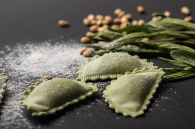 siyah masa üzerinde yeşil ravioli, adaçayı ve dağınık un ve çam fıstığı seçici odak