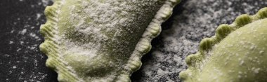 panoramic shot of green raw ravioli with flour on black table clipart