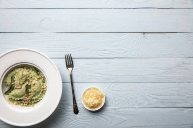 beyaz ahşap masa üzerinde çam fıstığı, adaçayı ve rendelenmiş peynir ile beyaz tabakta servis yeşil ravioli üst görünümü