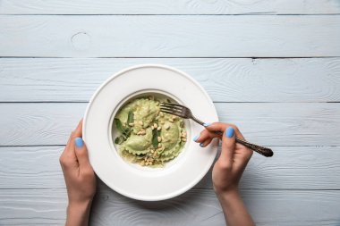 ahşap masada çam fıstığı ve adaçayı ile yeşil ravioli yiyen kadın kırpılmış görünümü