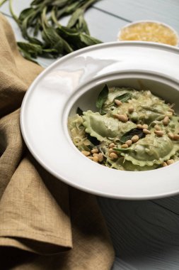 close up view of green ravioli served in white plate with sage, pine nuts and grated cheese near napkin clipart
