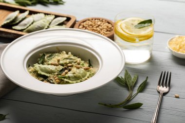 green ravioli with pine nuts, grated cheese and sage at wooden table near water with lemon clipart