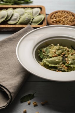 close up view of green ravioli served in plate with sage, pine nuts and grated cheese near napkin clipart