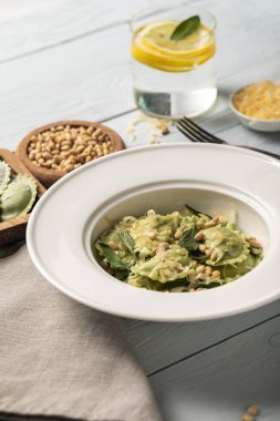 çam fıstığı, rendelenmiş peynir ve adaçayı ile yeşil ravioli yakın görünümü limon ile içecek yakın ahşap masada