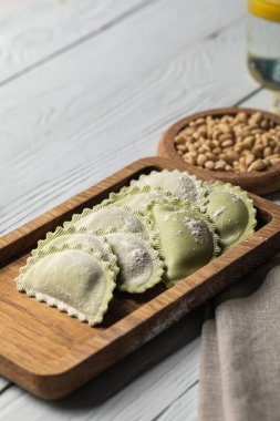 close up view of raw green ravioli with flour on wooden board near pine nuts clipart