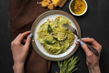 siyah ahşap masada adaçayı ve çam fıstığı ile lezzetli yeşil ravioli yiyen kadın üst görünümü
