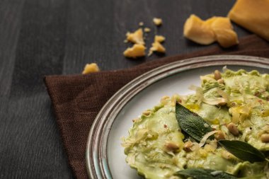 close up view of delicious green ravioli with sage, cheese and pine nuts served on black wooden table with brown napkin clipart