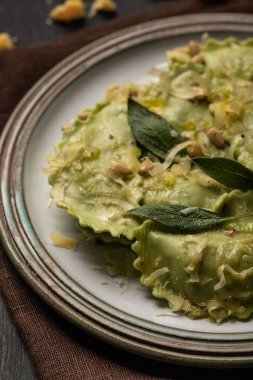 close up view of green ravioli with melted cheese, pine nuts and green sage leaves in retro plate clipart