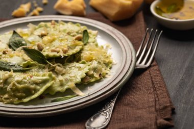erimiş peynir, çam fıstığı ve yeşil adaçayı yaprakları ile yeşil ravioli yakın görünümü çatal ile peçete üzerinde retro plaka