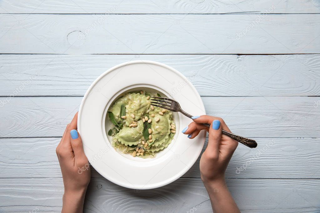 cropped view of woman eating green ravioli with pine nuts and sage at wooden table