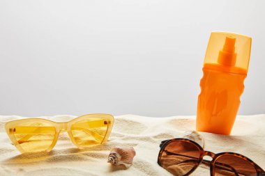 yellow and brown sunglasses and sunscreen in orange bottle on sand on grey background clipart
