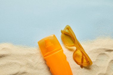 kum ile mavi arka plan üzerinde güneş gözlüğü yakınında turuncu şişe güneş kremi üst görünümü